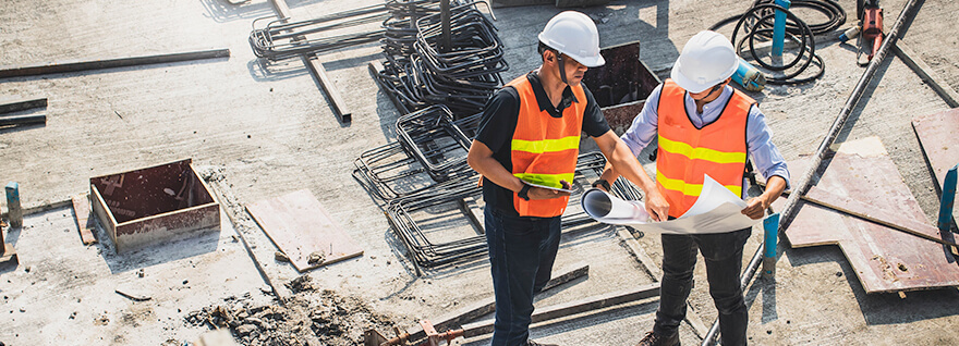 an overhead view of two men in safety gear reviewing plans while on a construction jobsite.