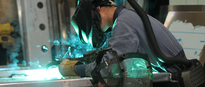 a Welder with a welding mask and gloves on illuminated with blue light from working on a project.