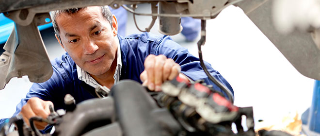 an Indigenous male Automotive Service Technician working on a vehicle.