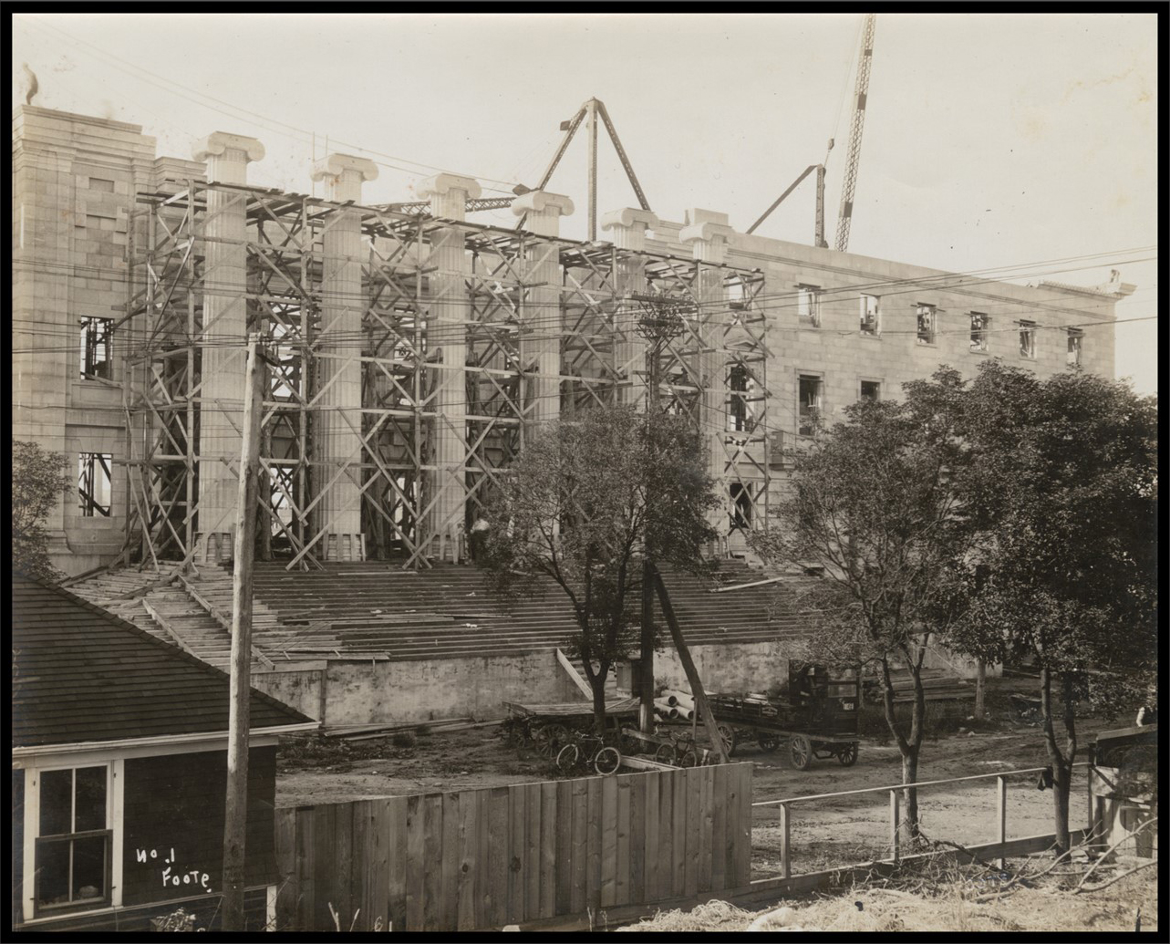 Photo of steps and stone columns under contruction. A house, bicycles, and trees are in the foreground adjacent to the construction.