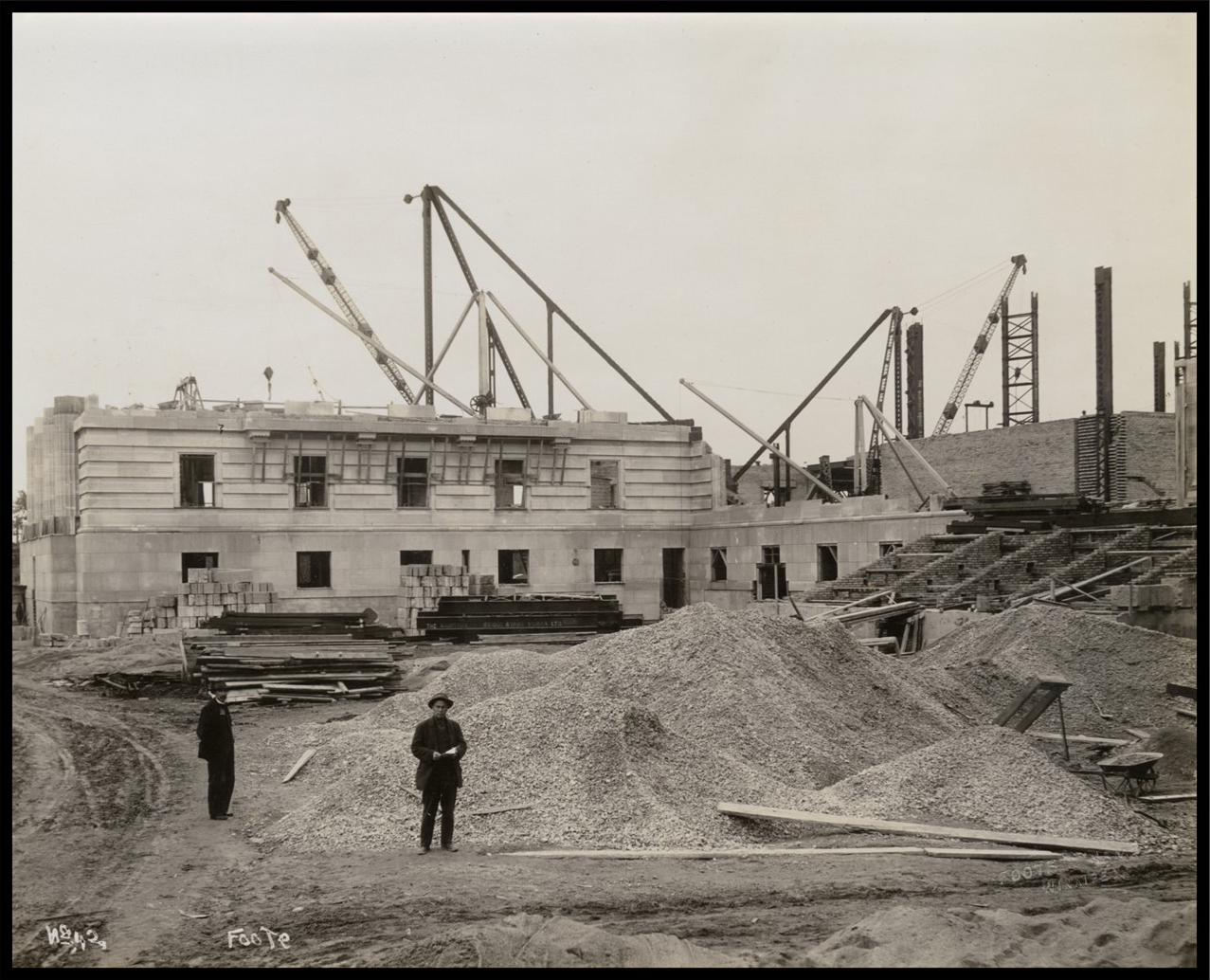 Exterior of the building at the ground level with two men standing next to a large pile of gravel.