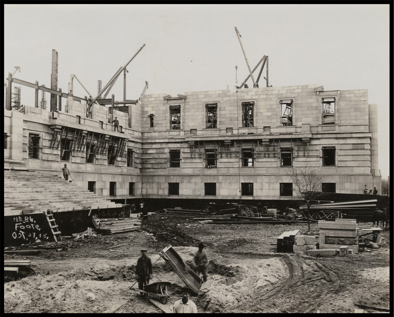 Exterior of the partially completed building at the ground level with several workers standing on different levels.
