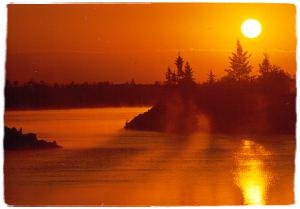 Image of a sunset over a lake with trees in the background.
