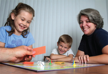 two children and a woman playing a board game smilng